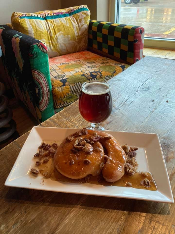 glass of light stout beer with a pecan maple stuicky bun